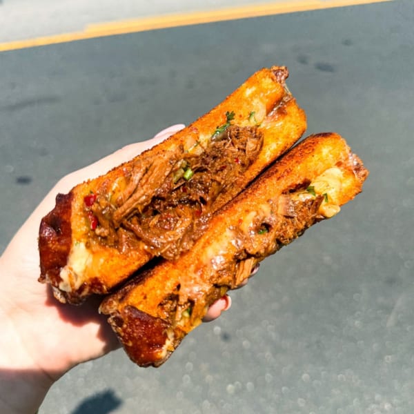 A hand holds two halves of a golden-brown Mexican birria quesadilla, filled with shredded meat and cheese.
