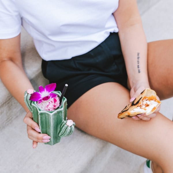 Person holding a cactus-shaped drink with a pink orchid and a dessert taco.
